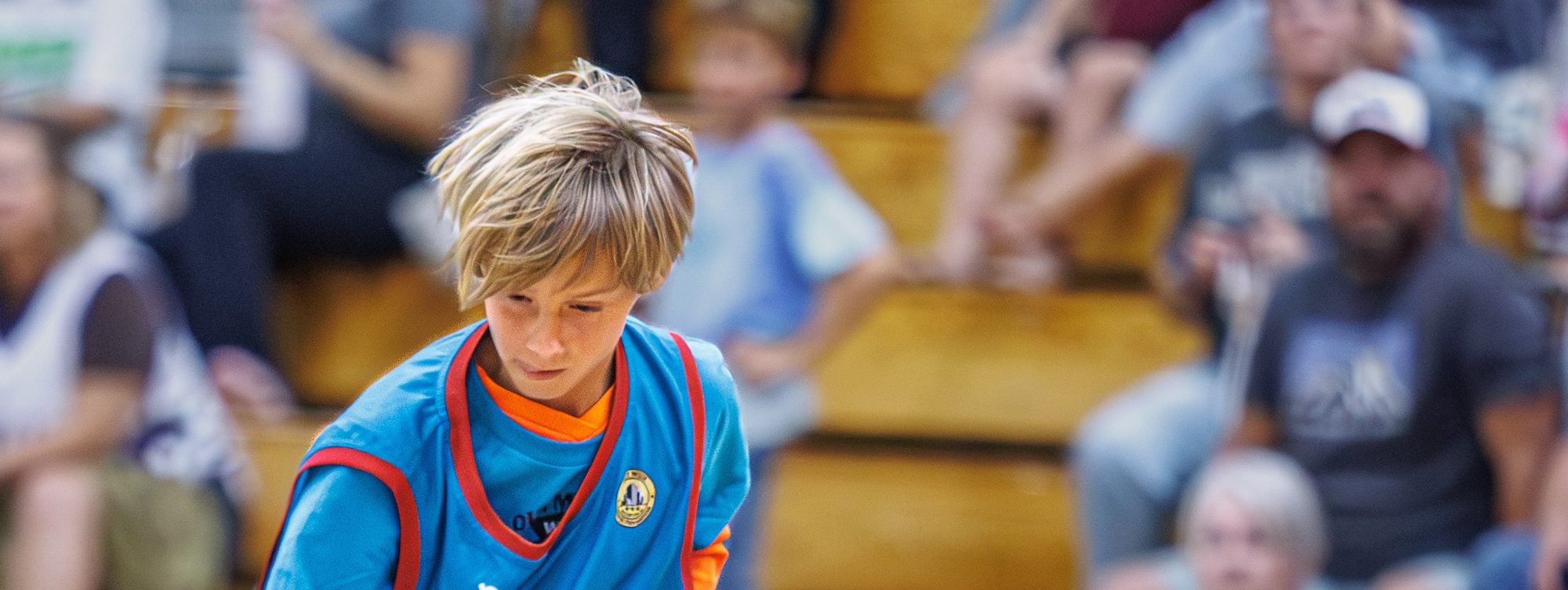 A kid in an oversized Sharks jersey dribbling in front of the bleachers