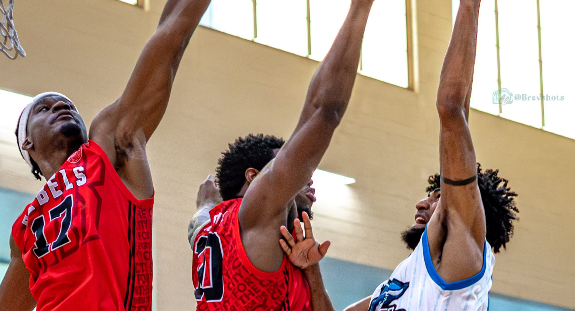 A Sharks player goes up for a rebound against two defenders in a full gym