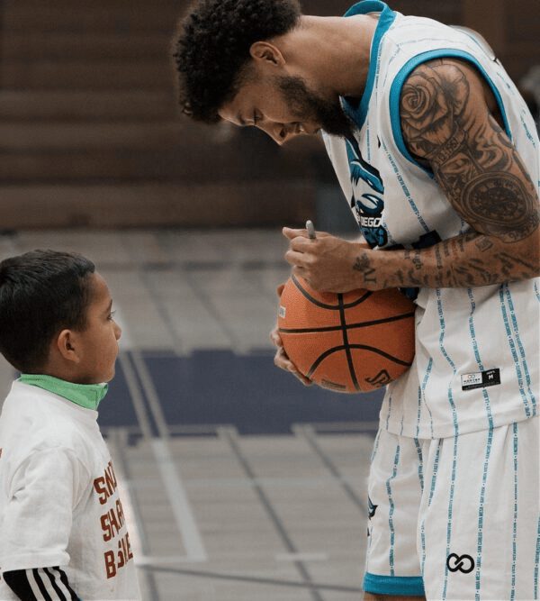 A Sharks player signing a basketball for a young fan