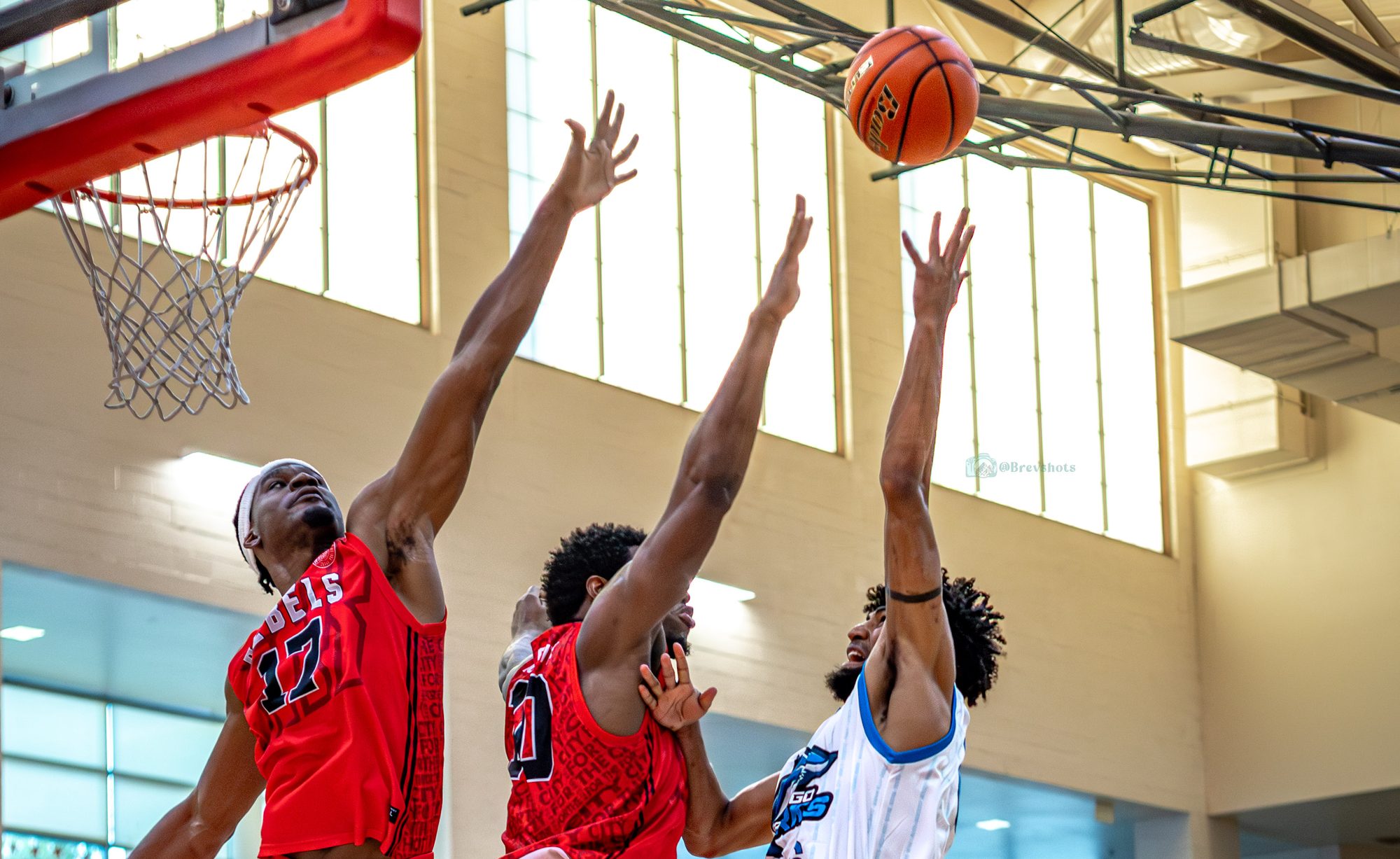 Three players reach for a rebound under the rim in a full gym